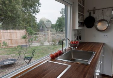 Stovetop with cutting board in place. Countertops are 2” walnut butcher block sourced from a local Mennonite planing mill (as were the walnut floors). The kitchen also features a full size microwave oven that also functions as a convection oven for baking.